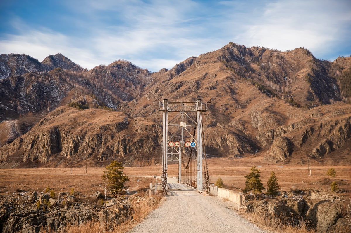A quiet bridge on a dirt road leading toward vast mountains at golden hour